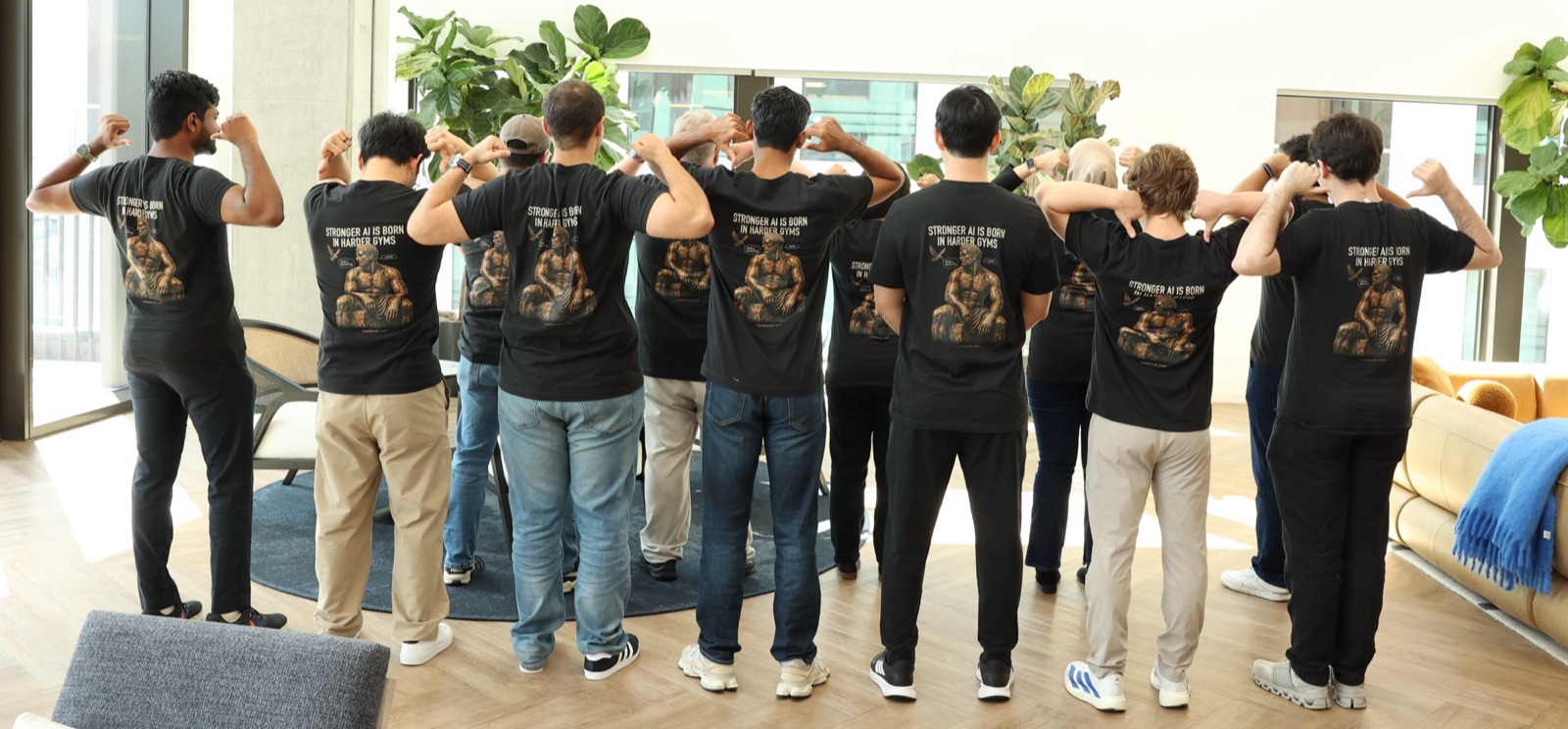 A large group of Collinear team members in matching black 'Harder Gyms' t-shirts, fist-bumping in an office lounge with large windows.