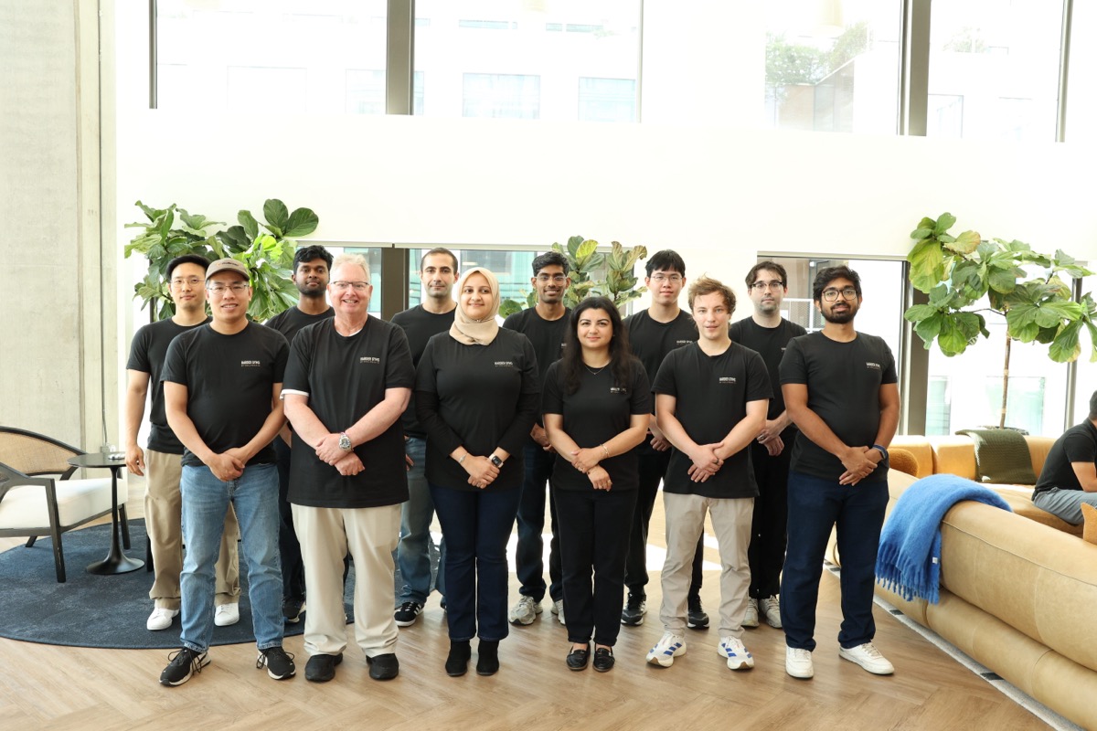 The Collinear team standing together in matching 'Harder Gyms by Collinear AI' t-shirts in front of large windows and potted plants.