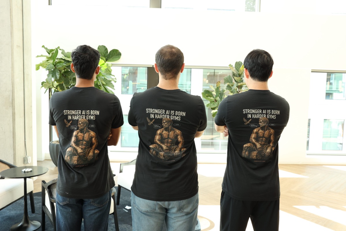 Three team members standing with arms crossed, backs to the camera, wearing matching 'Stronger AI is born in harder gyms' t-shirts.